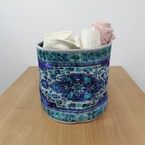 May include: A blue and white patterned fabric storage basket with a gray trim. The basket is filled with white and pink towels.