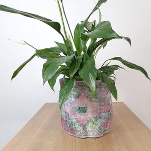May include: A green peace lily plant in a pink and green patterned fabric planter.