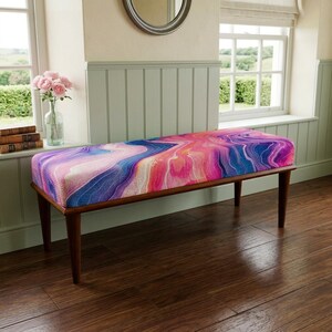 May include: A rectangular bench featuring a vibrant, multi-colored marble-like pattern in shades of pink, purple, and blue. The bench is supported by four tapered wooden legs in a dark brown finish, providing a stable base for the upholstered seat.