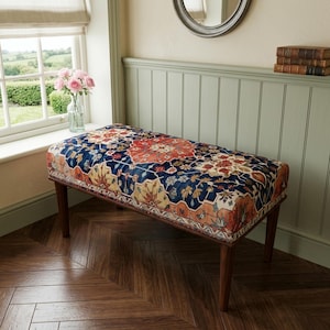 May include: A rectangular upholstered bench featuring a vibrant, multi-colored Persian-style rug pattern in shades of deep blue, orange, and cream. The bench is supported by four tapered, dark brown wooden legs and has a flat, padded top surface.