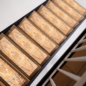 May include: A set of six patterned stair treads in beige and brown tones with a floral design. The treads are made of a soft, durable material and are designed to help prevent slips and falls on stairs.