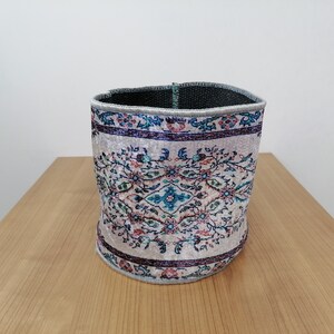 Könnte beinhalten: Ein zylindrischer Aufbewahrungskorb mit weißem Hintergrund und einem bunten Blumenmuster. Der Korb ist aus Stoff und hat ein schwarzes Stofffutter.