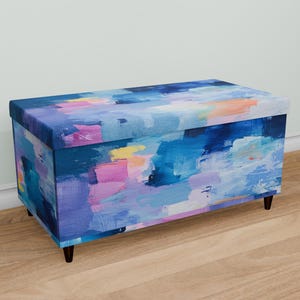 May include: A blue, pink, and yellow abstract patterned storage ottoman with black legs.
