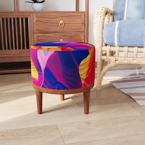 May include: A round ottoman featuring a vibrant, abstract pattern with swirling waves of deep blue, magenta, bright yellow, and orange. The seat is supported by four tapered wooden legs in a medium brown finish, providing a stable base.