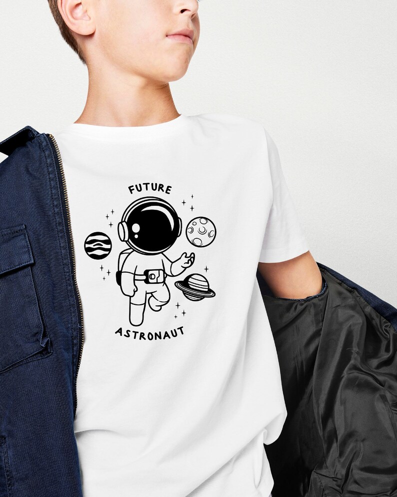 Puede incluir: Camiseta blanca con una ilustraci&oacute;n en blanco y negro de un astronauta, planetas y estrellas. El texto "FUTURE ASTRONAUT" est&aacute; impreso en la camiseta.