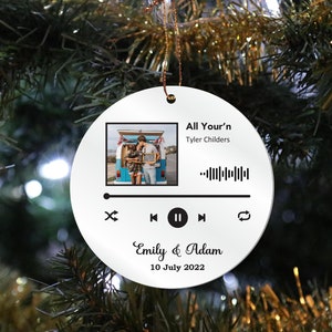 Könnte beinhalten: Runder weißer Weihnachtsbaumschmuck mit einem Musikplayer-Design. Der Anhänger zeigt ein Foto eines Paares, den Songtitel "All Your'n" von Tyler Childers, einen Barcode, Play-, Pause- und Skip-Buttons sowie den Text "Emily & Adam 10. Juli 2022".