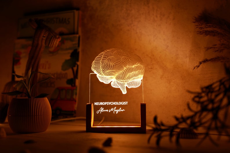 May include: A 3D printed brain-shaped night light with a wooden base. The light is illuminated and the text "NEUROPSYCHOLOGIST Alan Maglan" is engraved on the base.