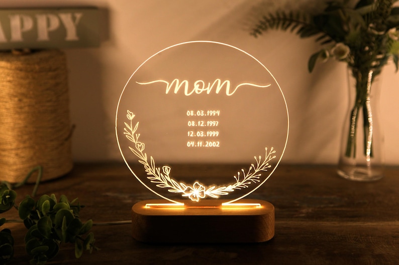May include: A round, clear acrylic night light with a wooden base. The light features a floral design and the word "mom" with dates inscribed below.
