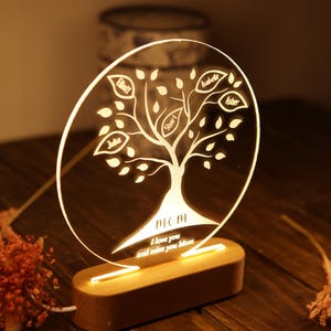 May include: A wooden base with a clear acrylic circle on top. The circle has a tree design with leaves and names inscribed on the leaves. The text "MOM I love you and miss you Mom" is inscribed at the bottom of the circle. The base has a light that illuminates the circle.