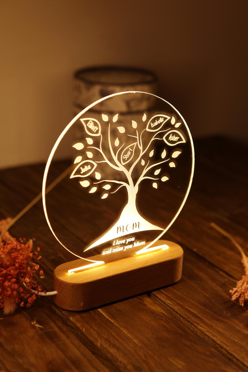 May include: A wooden base with a clear acrylic circle on top. The circle has a tree design with leaves and names inscribed on the leaves. The text "MOM I love you and miss you Mom" is inscribed at the bottom of the circle. The base has a light that illuminates the circle.