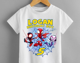 Könnte beinhalten: Weißes T-Shirt mit Spiderman-Motiv. Das Shirt hat ein blaues und weißes Spinnennetz-Design mit drei Spiderman-Charakteren. Der Text "LOGAN BIRTHDAY BOY" ist in gelben Buchstaben auf dem Shirt gedruckt. Die Zahl "5" ist in Gelb auf dem Spinnennetz gedruckt.