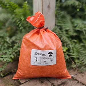 May include: An orange woven plastic bag containing Akadama hard medium grit soil. A white label on the front features the text Akadama, a bonsai tree icon, a small sheep logo, and the text 1 GAL, $25, REFILLABLE BAG, BAGGED IN HOUSE.