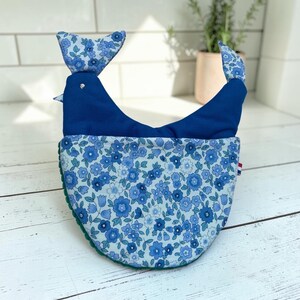 Peut inclure: Un gant de cuisine en tissu en forme d'oiseau, composé d'une partie supérieure bleu foncé uni et d'une partie inférieure à motif de fleurs bleu clair et bleu foncé. Le gant a une tête et une queue, avec un dessous texturé vert.