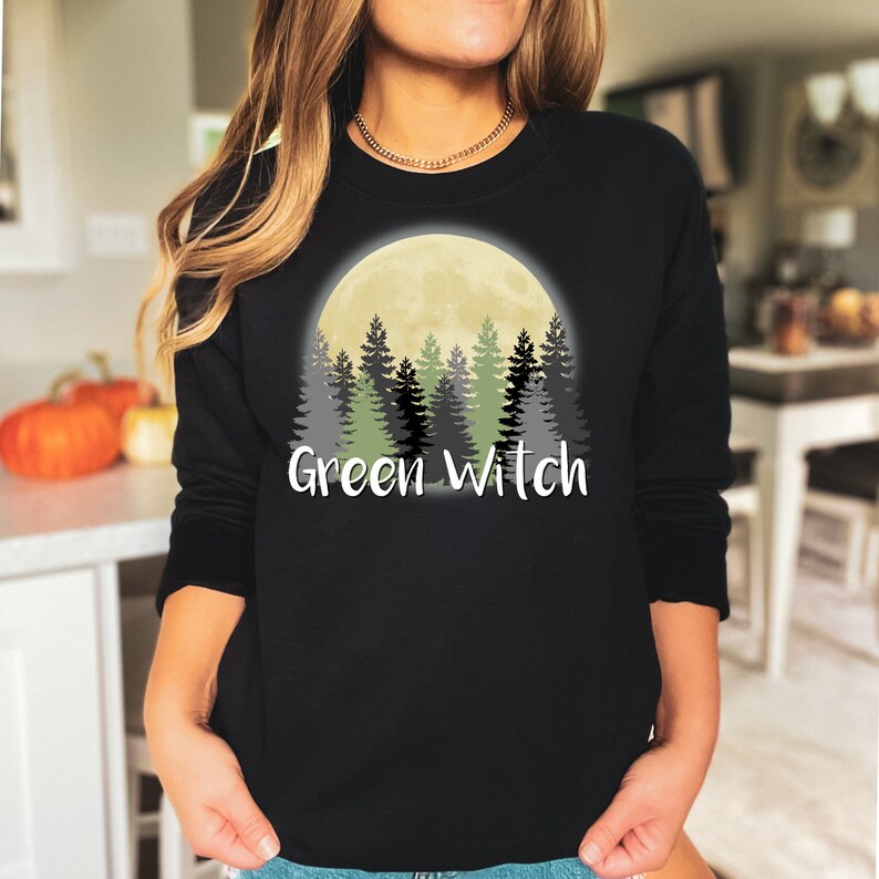 May include: Black sweatshirt with a graphic of a full moon and a forest silhouette. The text "Green Witch" is printed below the graphic.