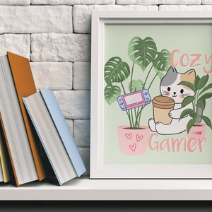 May include: A framed print with a cat illustration holding a coffee cup, with the text "Cozy Gamer." The image includes a video game console and potted plants. Books are visible on a shelf to the left.