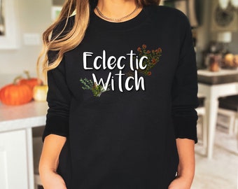Könnte beinhalten: Schwarzer Pullover mit dem Text "Eclectic Witch" in weißen Buchstaben und einem floralen Design.