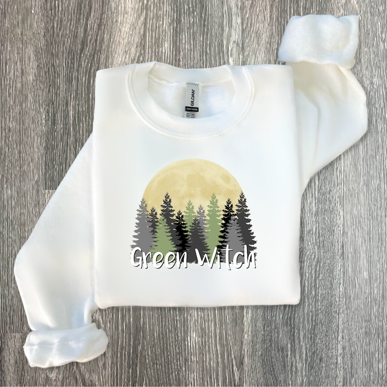 May include: White sweatshirt with a green, black, and gray forest scene with a yellow moon and the text "Green Witch" printed on the front.
