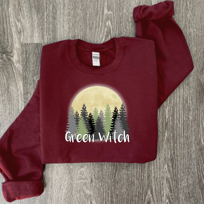 May include: A maroon sweatshirt with a graphic of a full moon and a forest silhouette. The text "Green Witch" is printed below the graphic.