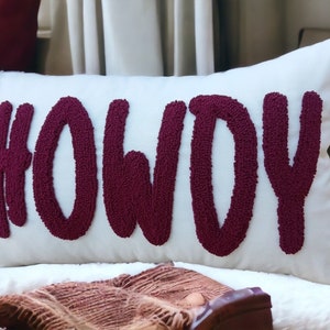 May include: White cushion with the word "HOWDY" embroidered in burgundy.