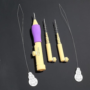 May include: A set of four tools for threading yarn through fabric. The tools are made of plastic and have a purple and yellow color scheme. The tools include a needle threader with a numbered dial, and three separate needle threaders with spring-loaded needles.
