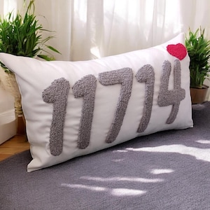 May include: White pillow with the number 1714 embroidered in gray and a small red heart in the top right corner.