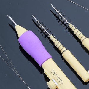 May include: Three needle threaders with spring-loaded mechanisms. The purple needle threader has a numbered scale on the side. The other two threaders are silver.