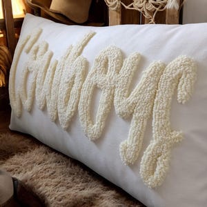 May include: A white rectangular cushion with the word "Cowboy" spelled out in raised white yarn.