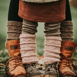 Könnte beinhalten: Nahaufnahme von zwei Paar gestrickten Beinstulpen, ein Paar in Braun und das andere in Rosa, getragen mit braunen Lederstiefeln. Die Stiefel haben den Schriftzug "Bugatti" aufgedruckt.