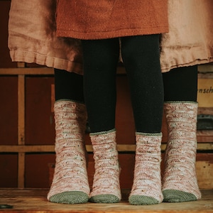 May include: Three pairs of pink and green patterned socks with a green cuff. The socks are worn by two people standing on a wooden surface.