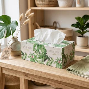 Peut inclure: Une boîte à mouchoirs rectangulaire ornée d'un motif botanique vert composé de diverses feuilles tropicales et du texte "LET'S GET LOST IN nature" imprimé sur le côté. La boîte est blanche avec une finition mate et contient des mouchoirs en papier.