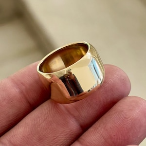 May include: A wide, polished gold ring with a rounded, barrel-like shape. The ring reflects light, creating a bright, shiny appearance. The ring is a simple, yet elegant piece of jewellery.