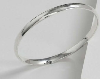 May include: A simple silver bangle bracelet with a smooth, polished finish. The bracelet is marked with the inscription "JNK".