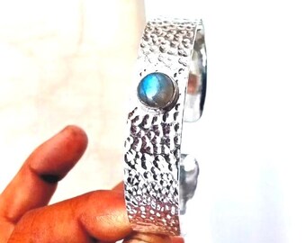 May include: A silver cuff bracelet with a hammered texture and a blue labradorite gemstone set in the centre.