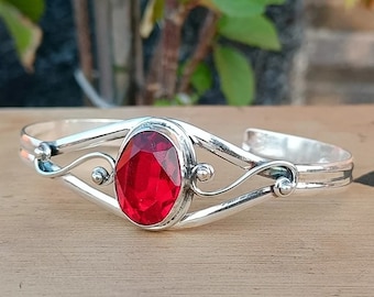 May include: A silver bangle bracelet with a red gemstone set in a decorative silver setting.