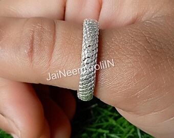 May include: A silver ring with a textured, woven design. The ring is shown on a finger.
