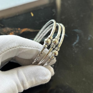 May include: Three silver bangles with a textured design and small round beads. The bangles are stacked on top of each other.