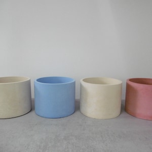 Peut inclure: Quatre pots de fleurs cylindriques de différentes couleurs. Les couleurs sont crème, bleu clair, crème et rose. Les pots sont en matériau mat et ont une finition lisse. Conviennent à une utilisation intérieure ou extérieure, idéaux pour les plantes.