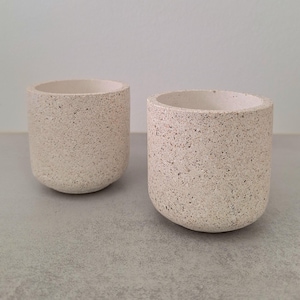 May include: Two small, white, speckled concrete planters. The planters are cylindrical with a rounded bottom.