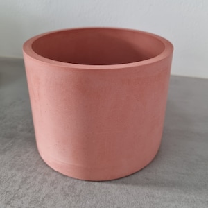Peut inclure: Un pot rond en béton de couleur rose clair. Le pot est lisse et présente une surface légèrement texturée.