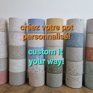Può includere: Una collezione di vasi in terrazzo colorati di diverse dimensioni. I vasi sono impilati e disposti in fila. Il testo "créez votre pot personnalisé! custom it your way!" è visualizzato al centro dell'immagine.