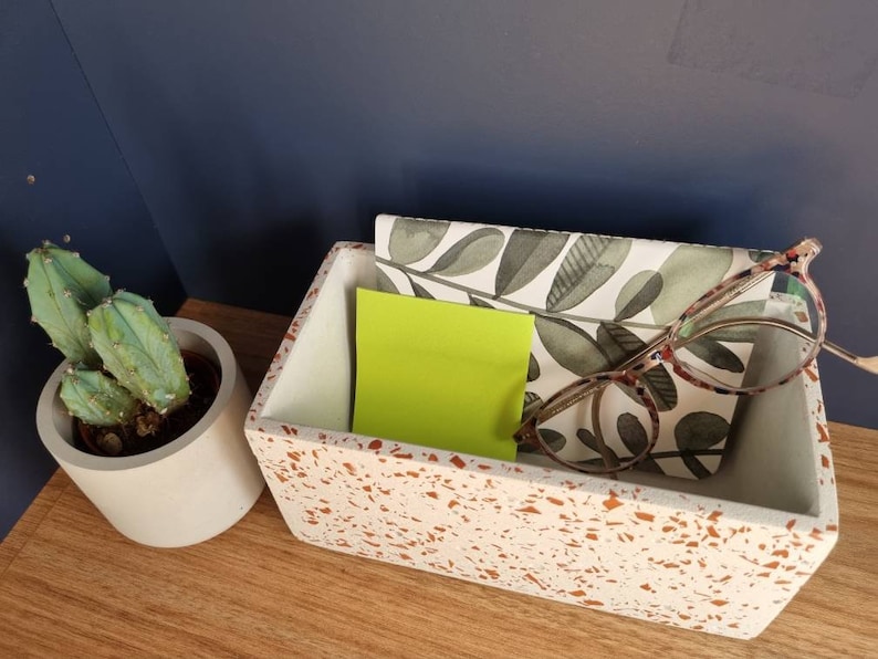 May include: A white rectangular terrazzo tray with a green and white patterned paper inside. The tray contains a yellow sticky note and a pair of spectacles.