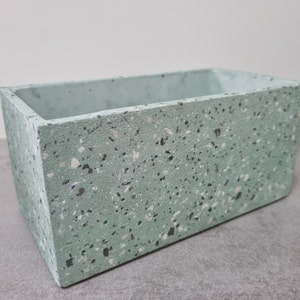 May include: A rectangular terrazzo planter in a light green colour with white and grey flecks. The planter is made of concrete and has a smooth finish.