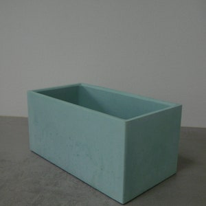 May include: A light blue rectangular concrete planter. The planter is made of a rough, textured material.