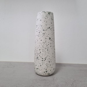 May include: A white ceramic vase with a speckled green and white pattern. The vase has a tall, slender shape.
