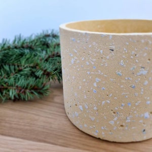Könnte beinhalten: Ein gelber Topf mit weißen und blauen Flecken. Der Topf ist aus Beton und hat eine gesprenkelte Oberfläche.