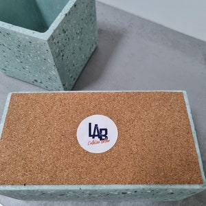 May include: A light blue concrete planter with a speckled finish. The planter has a cork base and a white sticker with the text "LAB L'atelier Beton".
