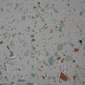 May include: A close-up of a white surface with small, colourful flecks of terrazzo. The flecks are mostly beige, brown, and blue.