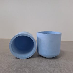 Peut inclure: Deux pots en céramique bleu clair, l'un retourné pour montrer l'intérieur. Les pots sont de conception simple et moderne.