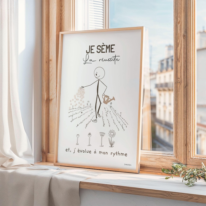 Un bonhomme bâton minimaliste et esthétique sème des graines dans un jardin. Il disperse soigneusement des graines. Des fleurs épanouies et d’autres en train d’éclore illustrent le titre ‘Je sème la réussite’. Affiche encadrée en bois posée sur un rebord de fenêtre orné de rideaux en lin beige. Le cadre est légèrement incliné.