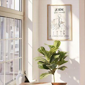 Un bonhomme bâton minimaliste et esthétique sème des graines dans un jardin. Il disperse soigneusement des graines. Des fleurs épanouies et d’autres en train d’éclore illustrent le titre ‘Je sème la réussite’. L'affiche est présentée dans un cadre accroché sur un mur blanc à côté d'une fenêtre ouverte. La pièce est ensoleillée et il y a un bureau et une grande plante verte.